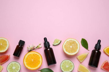 Flat lay composition with bottles of citrus essential oil on pink background. Space for text
