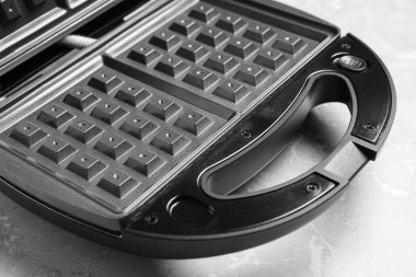 Modern waffle iron on grey marble table, closeup