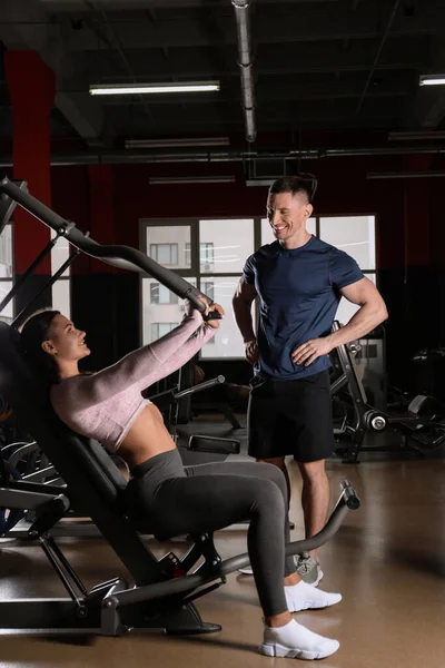 Trainer met jonge vrouw uit te werken op de borst pers machine in g — Stockfoto
