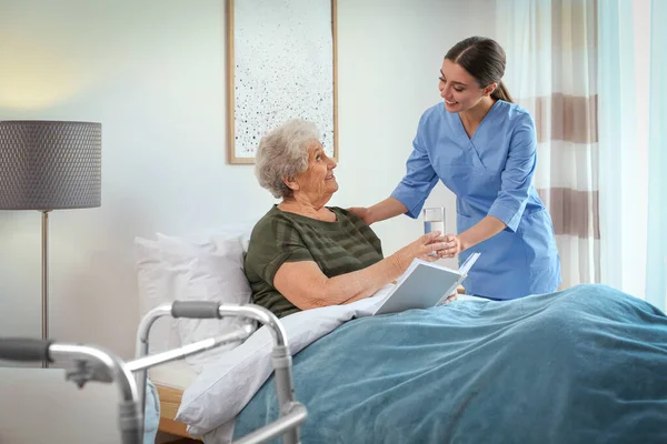 Care worker giving water to elderly woman in geriatric hospice