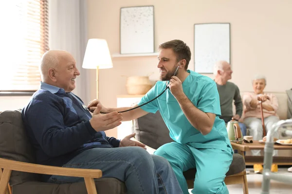 Care worker examining elderly patient with stethoscope in geriat — 스톡 사진