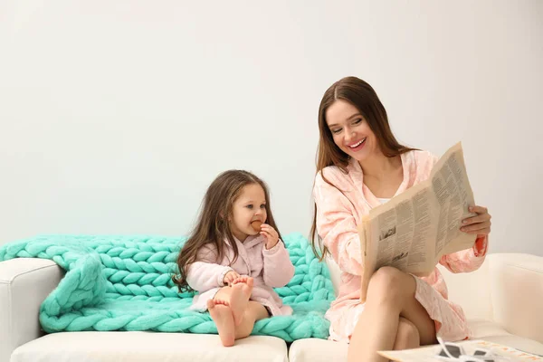 Madre e hija en albornoces sentadas en el sofá —  Fotos de Stock
