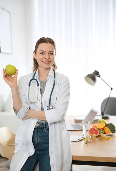 Nutritionist with fresh apple near desk in office — Stok fotoğraf