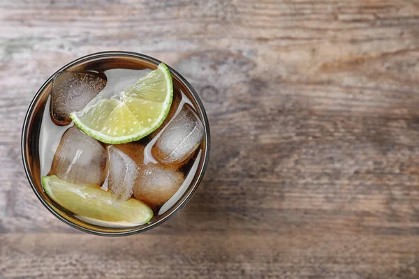 Glass of fresh Cuba Libre cocktail on wooden table, top view. Sp — Stock Photo, Image