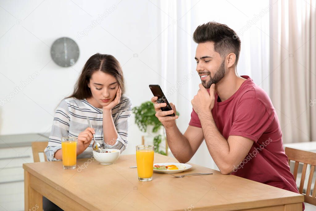 Young man preferring smartphone over his girlfriend at home