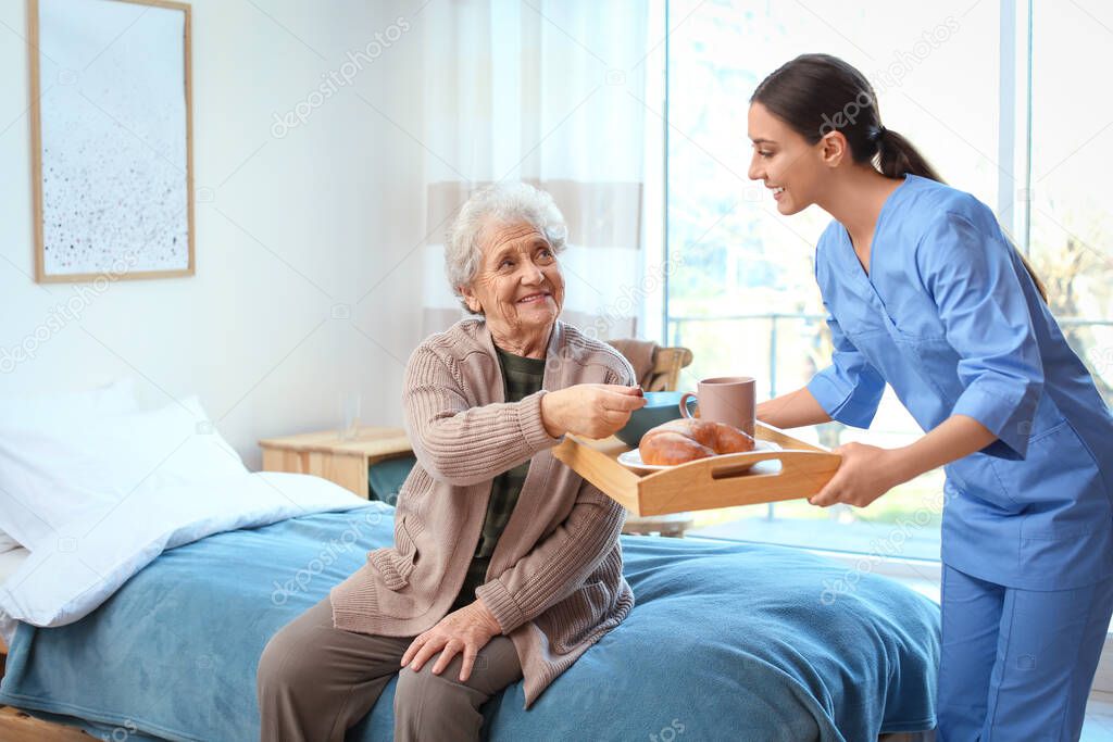 Care worker serving dinner for elderly woman in geriatric hospic