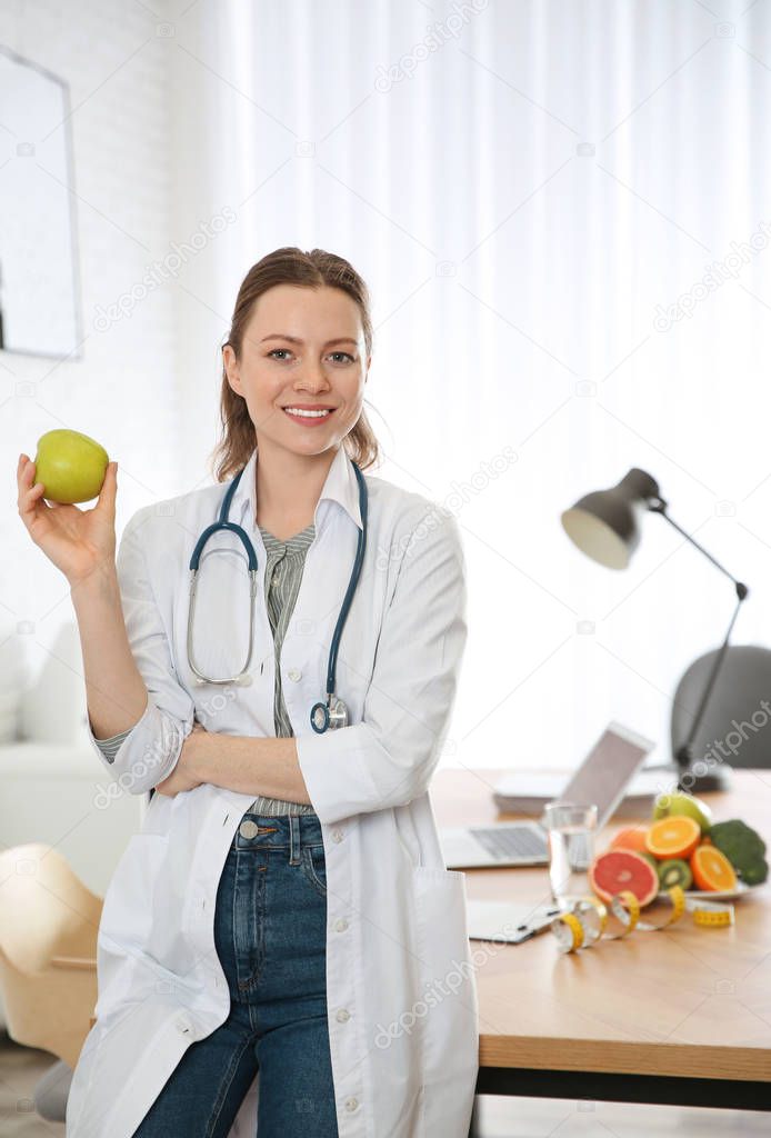 Nutritionist with fresh apple near desk in office