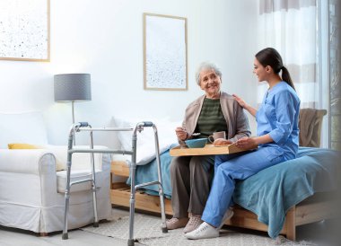 Care worker serving dinner for elderly woman in geriatric hospic clipart