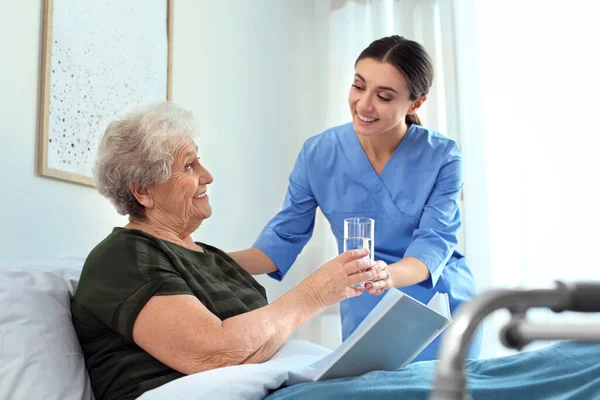 Pflegekraft versorgt ältere Frau in Altenheim mit Wasser — Stockfoto