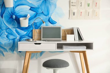 Stylish workplace with blue flowers painted on wall. Floral patt