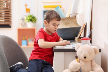 Little child painting at table in room