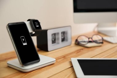 Cep telefonu ve ahşap masa üzerinde kablosuz şarj aleti olan akıllı saat.