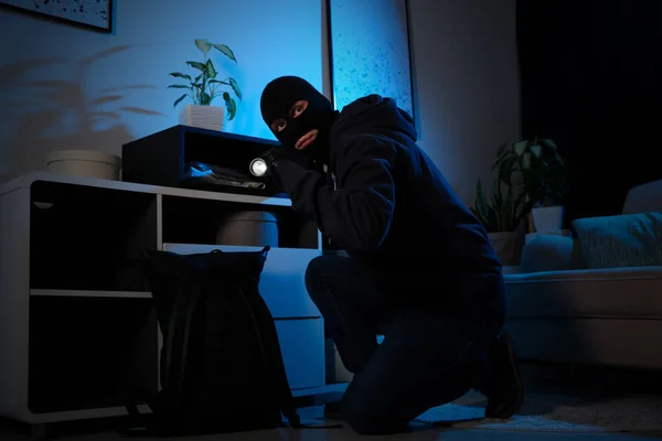 Thief with flashlight near steel safe indoors at night — 스톡 사진