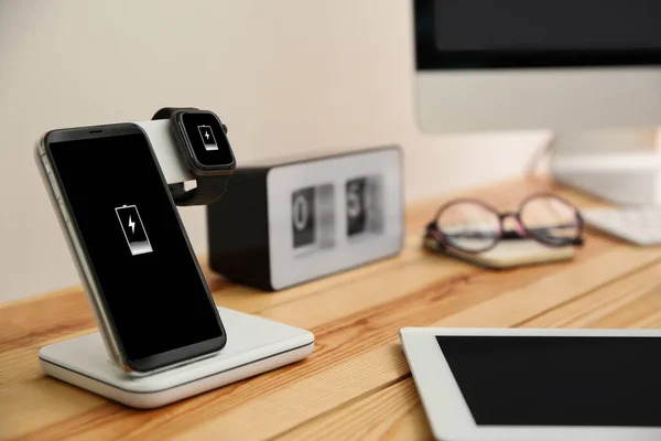 나무 탁자 위에 무선 충전기가 달린 휴대 전화와 스마트 워치 — 스톡 사진