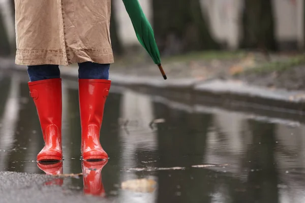 Жінка в гумових чоботях з парасолькою, що йде на відкритому повітрі на дощовому да — стокове фото