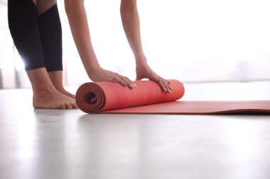 Yoga stüdyosunda paspası yerde yuvarlanan bir kadın.