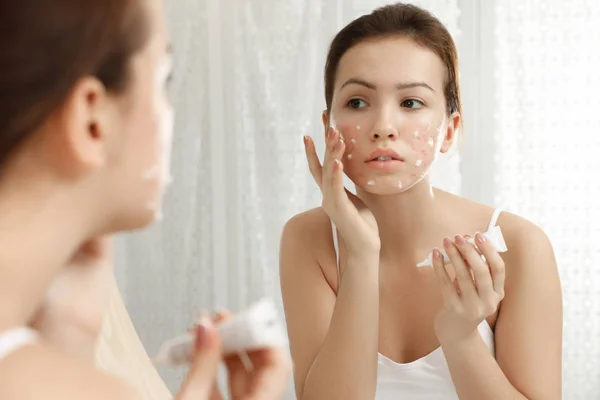 Chica adolescente con problemas de acné aplicando crema cerca del espejo en bathro — Foto de Stock