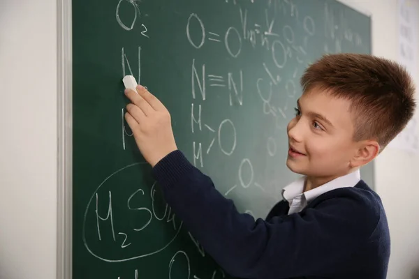 Schoolboy escrevendo fórmulas químicas em quadro-negro em sala de aula — Fotografia de Stock