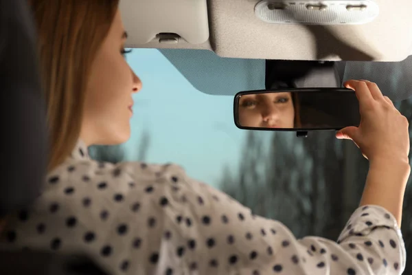 Mujer joven ajustando el espejo retrovisor en el coche, primer plano — Foto de Stock