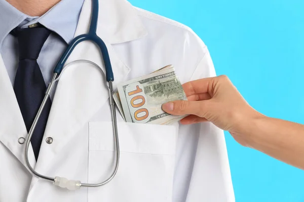 Patient putting bribe into doctor's pocket on light blue backgro — Stock Photo, Image