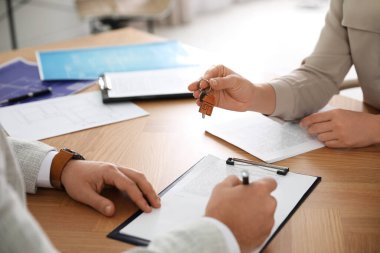 Real estate agent giving key with trinket to client in office, c