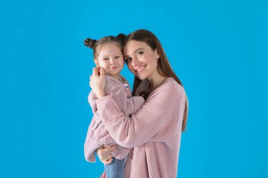 Young mother and little daughter on blue background
