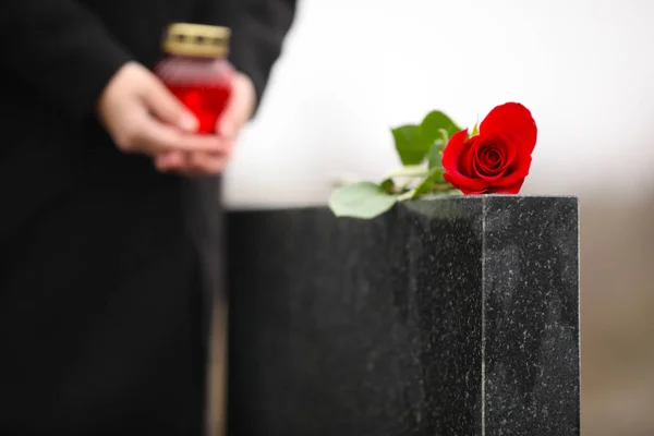 Femme avec bougie près de pierre tombale en granit noir à l'extérieur, focus o — Photo