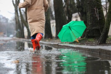 Woman in rubber boots running after umbrella outdoors on rainy d