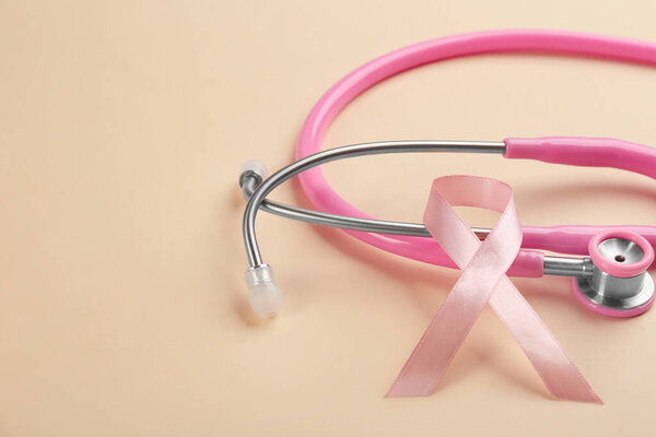 Pink ribbon and stethoscope on beige background, closeup. Breast