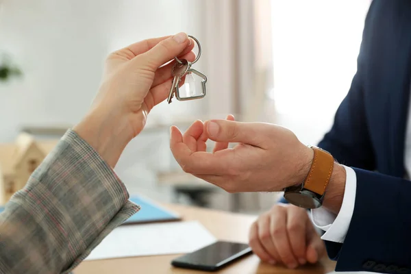 Real estate agent giving key with trinket to client in office, c — Stock Photo, Image