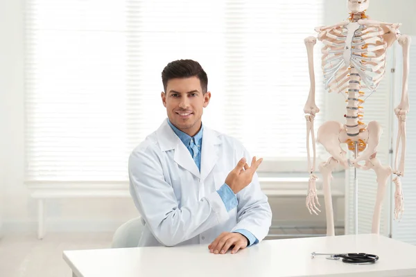Hombre ortopedista en la mesa cerca de esqueleto humano modelo en la oficina — Foto de Stock