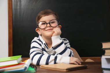 Cute little child wearing glasses at desk in classroom. First ti