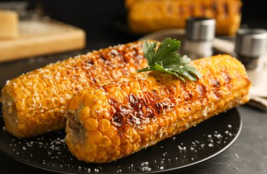 Delicious grilled corn cobs on black table, closeup