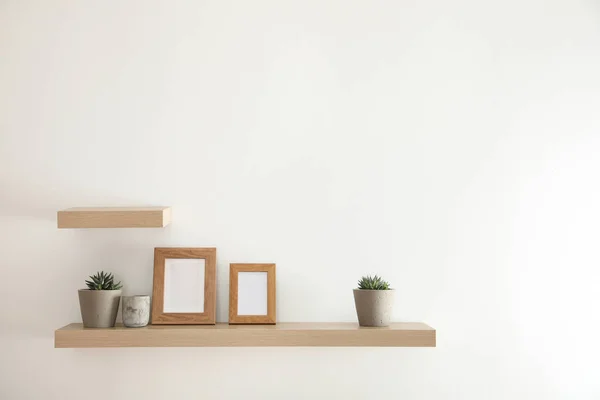 Prateleiras de madeira com plantas e molduras para fotos na parede leve — Fotografia de Stock