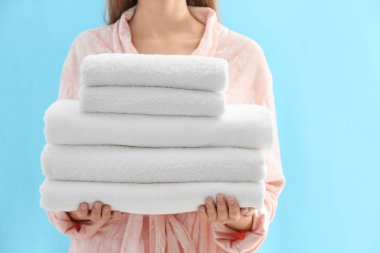 Woman holding stack of fresh clean towels on light blue backgrou