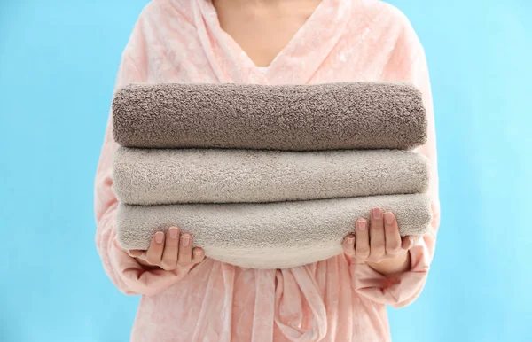 Woman holding stack of fresh clean towels on light blue backgrou — ストック写真