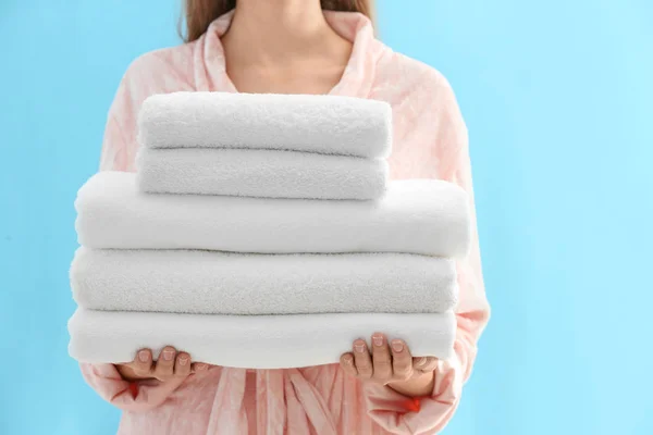 Woman holding stack of fresh clean towels on light blue backgrou — 스톡 사진