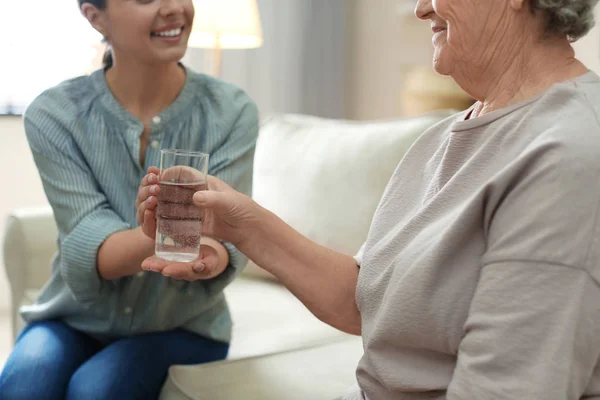 Mujer joven dando agua a anciana en el interior, primer plano. Senio. — Foto de Stock