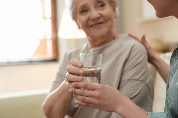 Jeune femme donnant de l'eau à une dame âgée à l'intérieur, se concentrer sur les mains — Photo