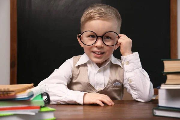 Cute little child wearing glasses at desk in classroom. First ti — ストック写真