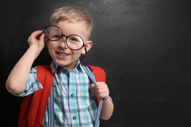 Funny little child wearing glasses near chalkboard, space for te