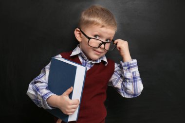 Cute little child wearing glasses near chalkboard. First time at