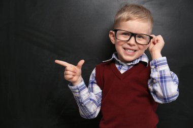 Cute little child wearing glasses near chalkboard. First time at