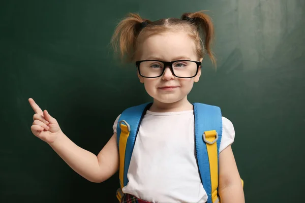 Cute little child wearing glasses near chalkboard. First time at — ストック写真