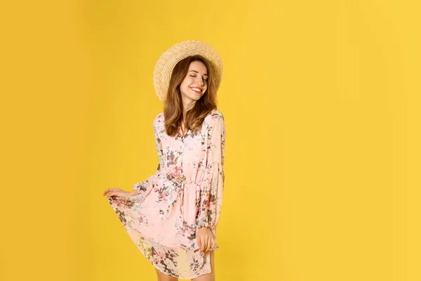 Mladá žena na sobě květinové šaty a slaměný klobouk na žluté b — Stock fotografie