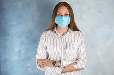 Yüzü açık mavi arka planda tek kullanımlık maskeli kadın
