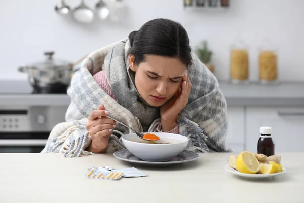 Doente jovem mulher comendo sopa para curar a gripe na mesa na cozinha — Fotografia de Stock