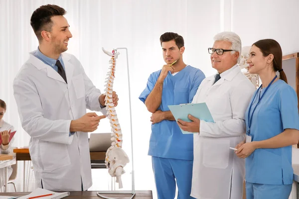 Medical students and professor studying human spine structure in classroom