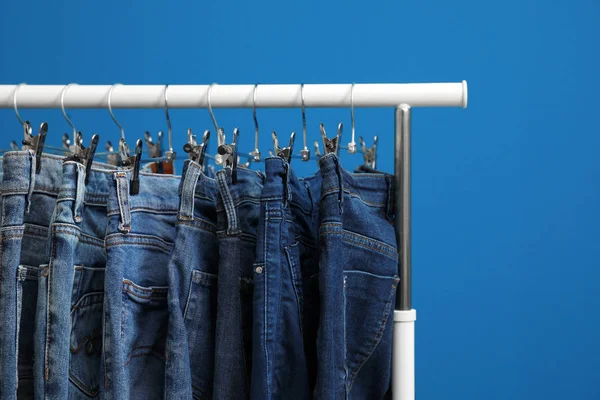 Rack with stylish jeans on blue background, closeup — Stock Photo, Image