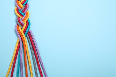Açık mavi arkaplanda örülmüş renkli iplerin üst görünümü, metin için boşluk. Birlik kavramı